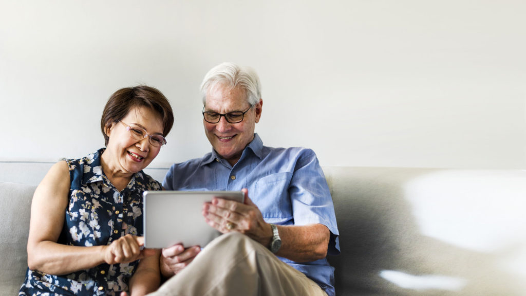 Senior couple sitting on sofa smiling at tablet