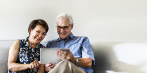Senior couple sitting on sofa smiling at tablet