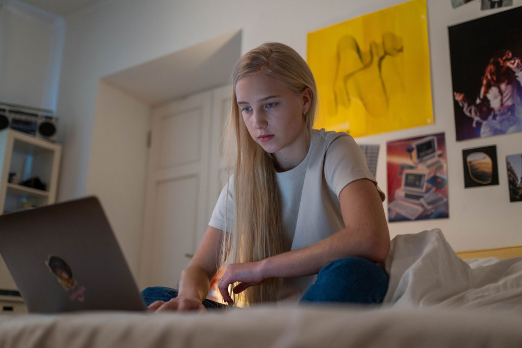 Young teen sitting on white bed with a laptop